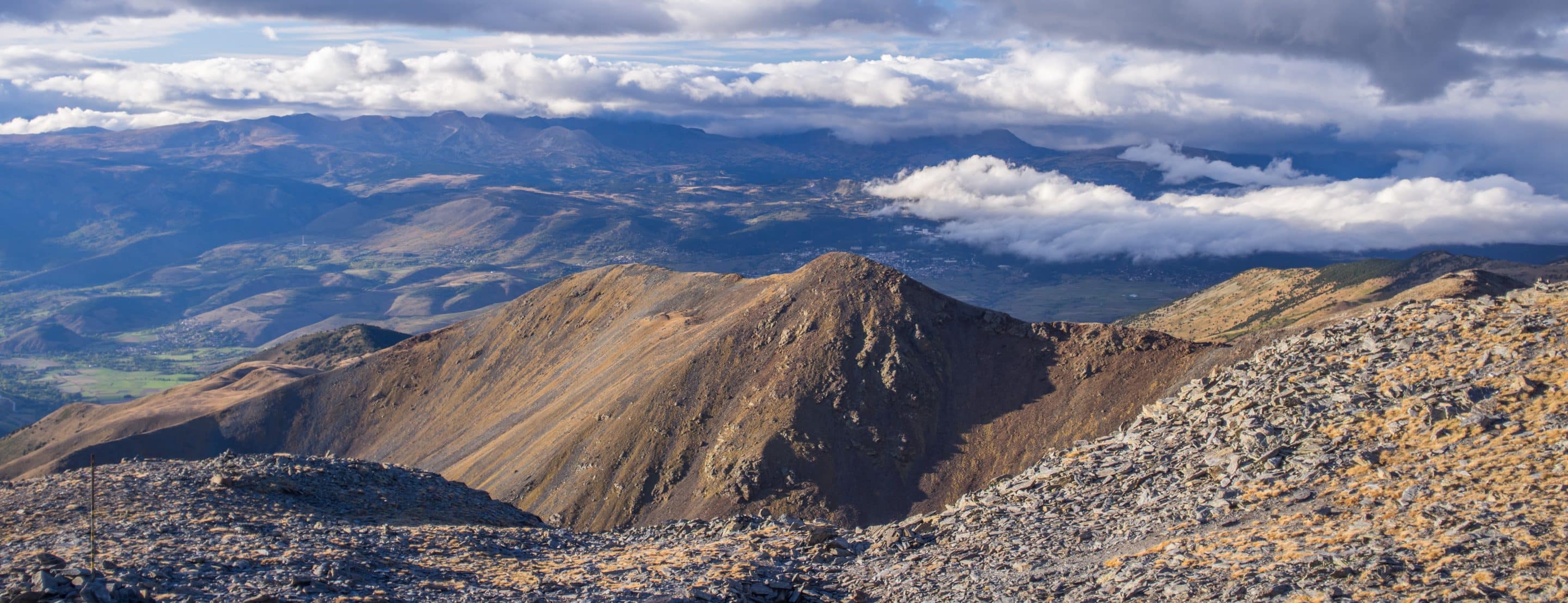 Vue panoramique du massif du Puigmal depuis Cotzé, dans les Pyrénées-Orientales, avec des nuages bas sur les vallées environnantes.