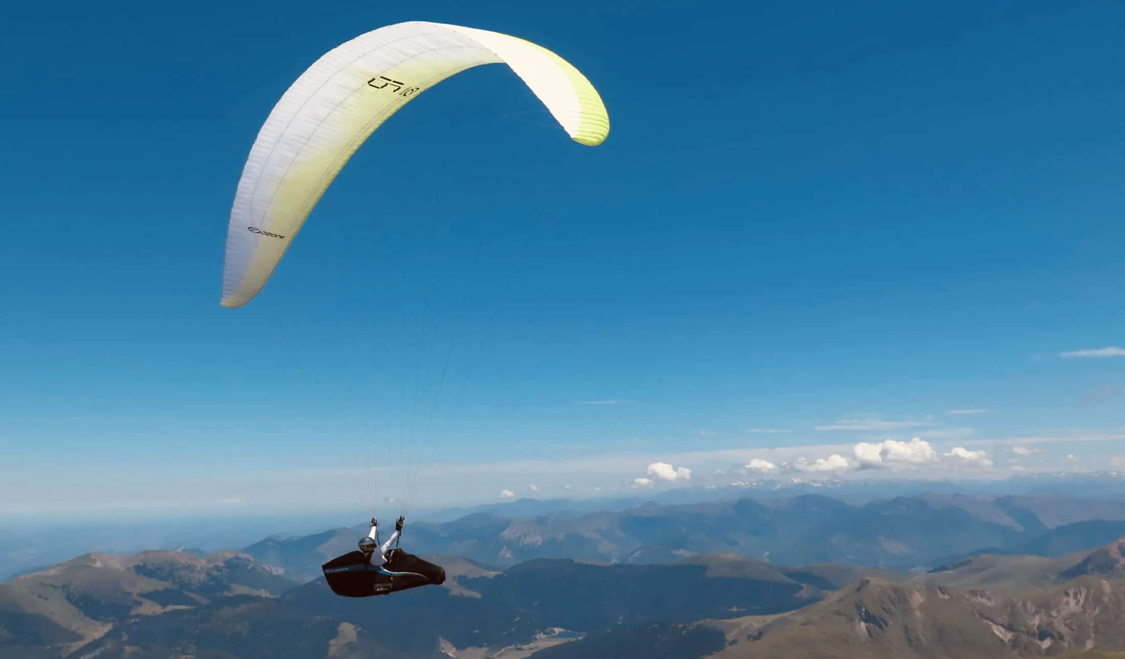 Un parapente blanc et jaune en vol au-dessus des montagnes de Sorède, dans les Pyrénées-Orientales, sous un ciel bleu dégagé