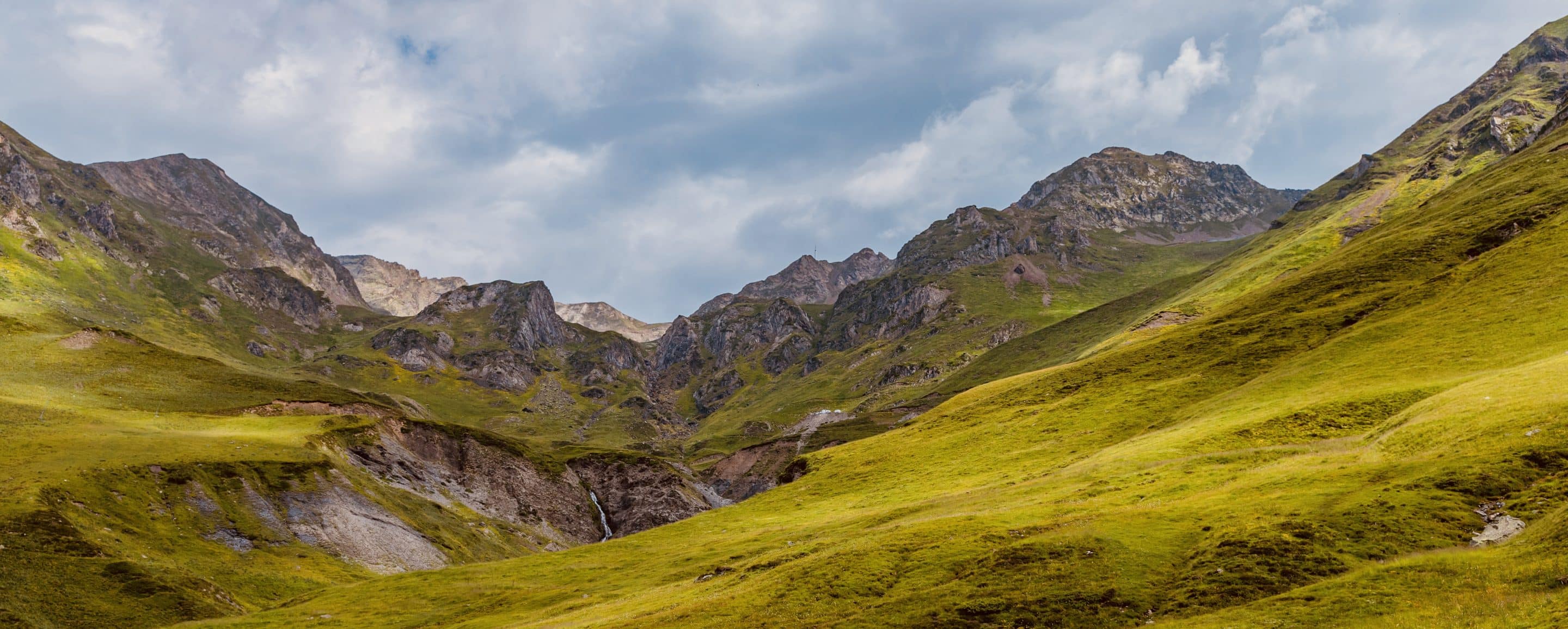 Paysage verdoyant et montagneux à Barèges-Tourmalet, dans les Hautes-Pyrénées, avec une cascade visible au centre.