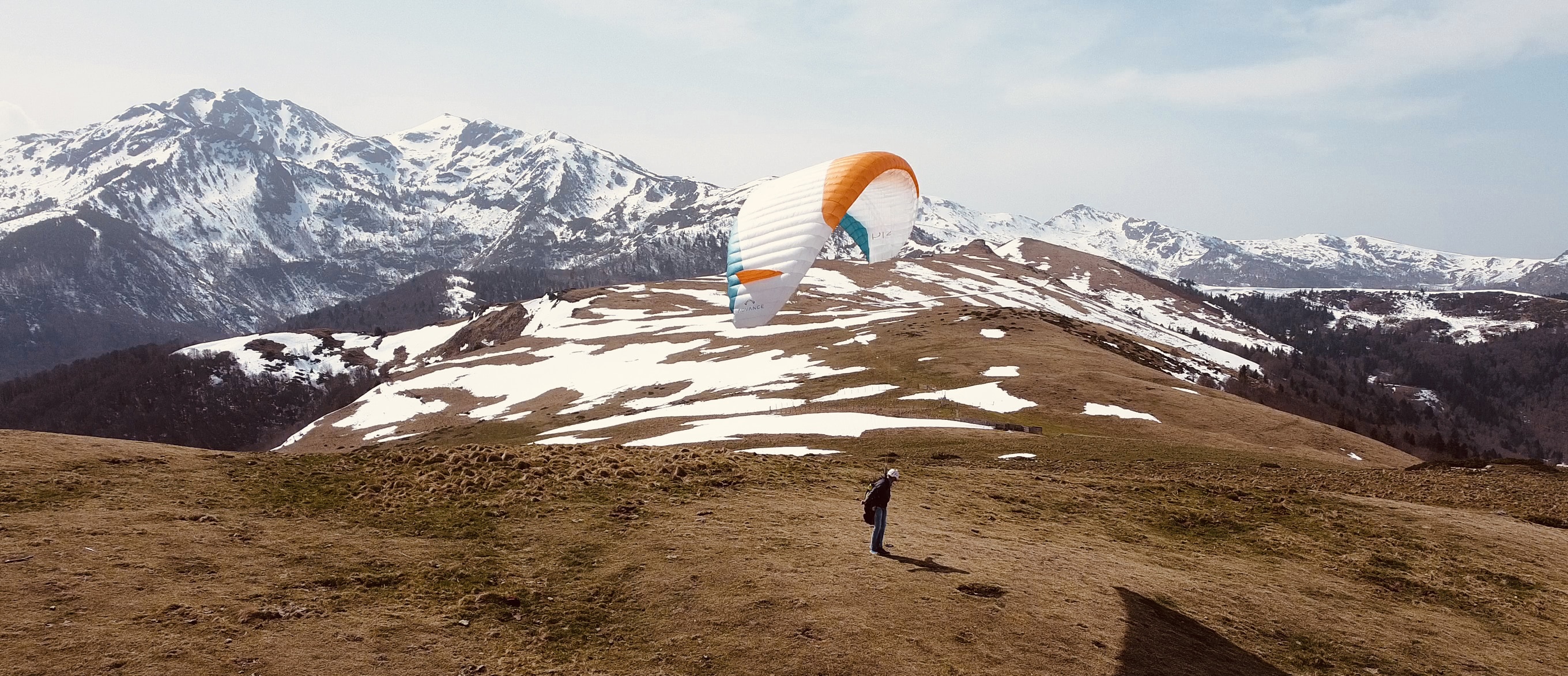 Parapente au décollage depuis le Roc de la Gourgue, près de Montségur en Ariège, avec les montagnes enneigées en arrière-plan.